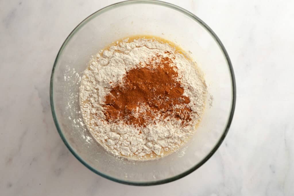 all purpose flour, baking powder and cinnamon on top of wet ingredients for waffles in a glass mixing bowl