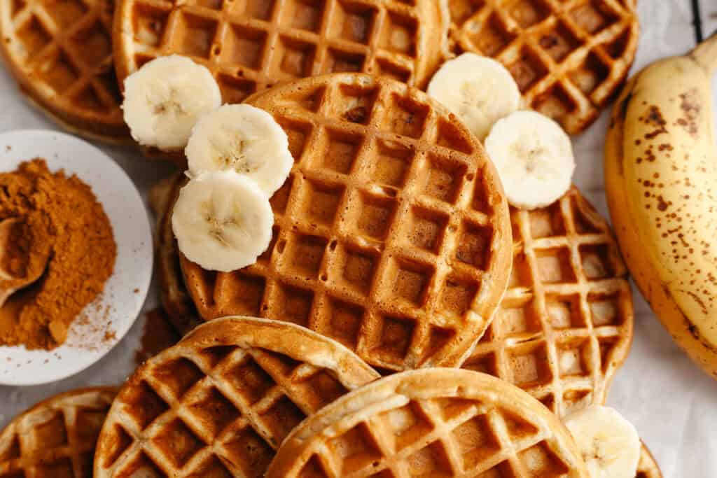 golden brown cooked banana waffles on a cutting board with slices of fresh banana on top