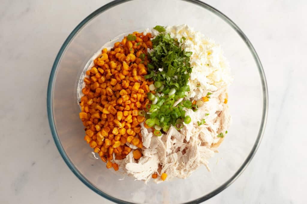 corn kernels, cotija cheese, cilantro and green onion added to a bowl with shredded chicken and sauce