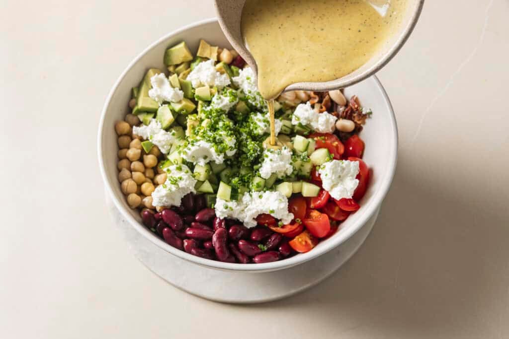 honey mustard being poured into the three bean chopped cobb salad