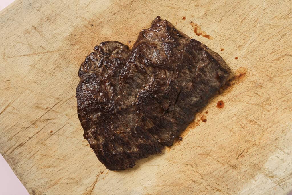 cooked flat iron steak cooling on a cutting board