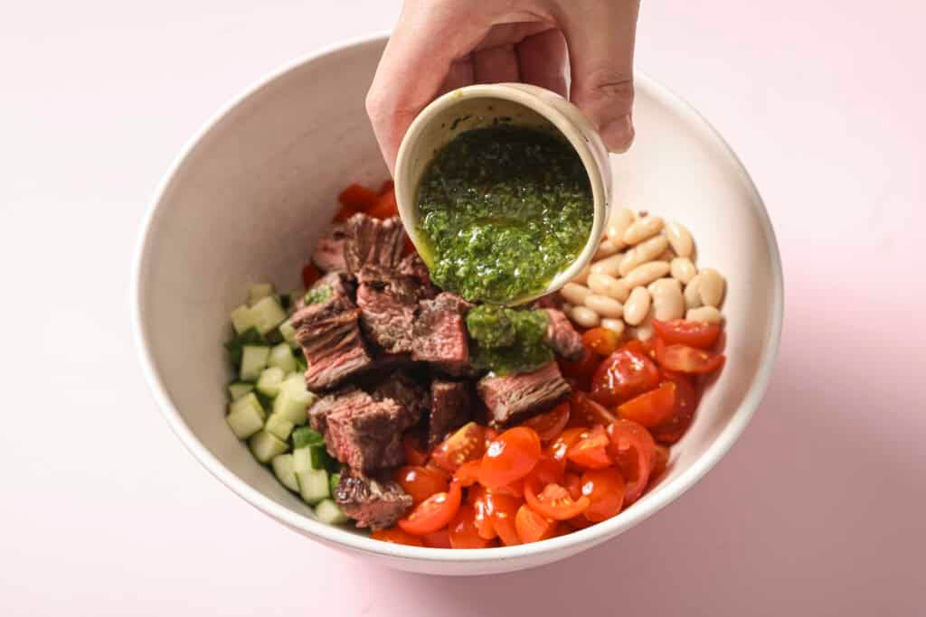 chimichurri dressing being added to the steak salad