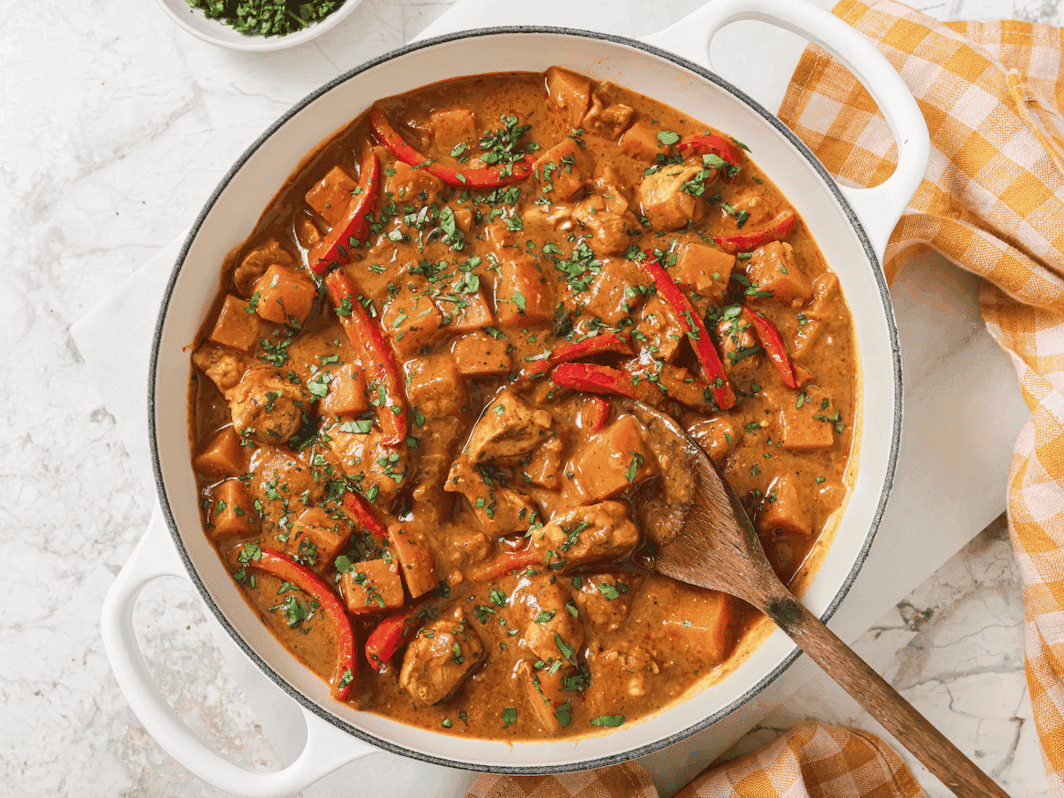pumpkin coconut chicken curry in a skillet with some cilantro on top and a wooden spoon in the skillet