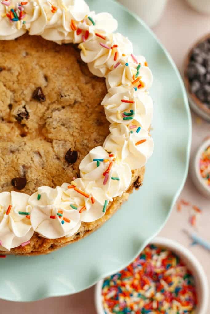 a layered cookie cake with icing on a plate, sprinkles in the background