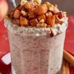 a glass filled with apple pie overnight oats with a spoon in them