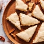maple pecan scones on a ceramic plate with pecans scattered on table