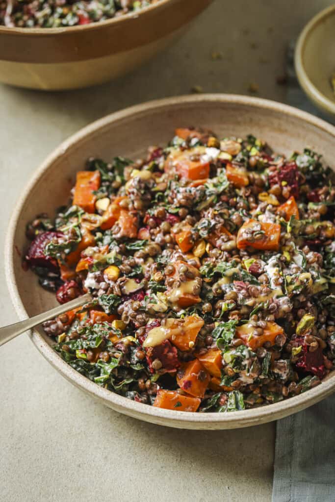 roasted beet and lentil chopped salad in a tan bowl with a spoon in it