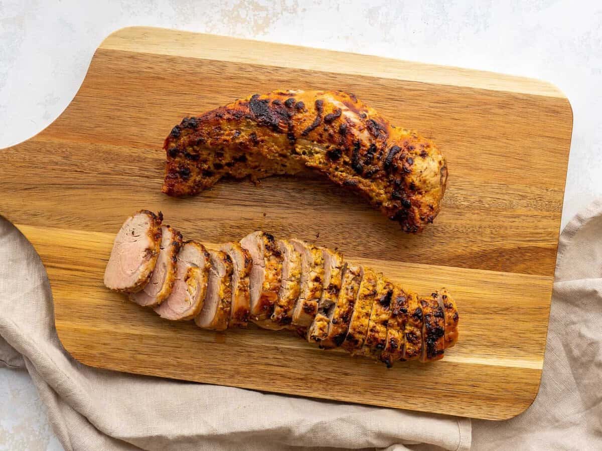 Two air fried pork tenderloins on a cutting board. One is whole and one is cut into slices