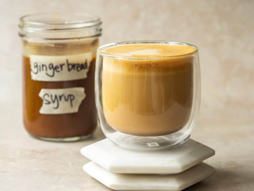 Gingerbread latte in a mug next to a jar of gingerbread syrup