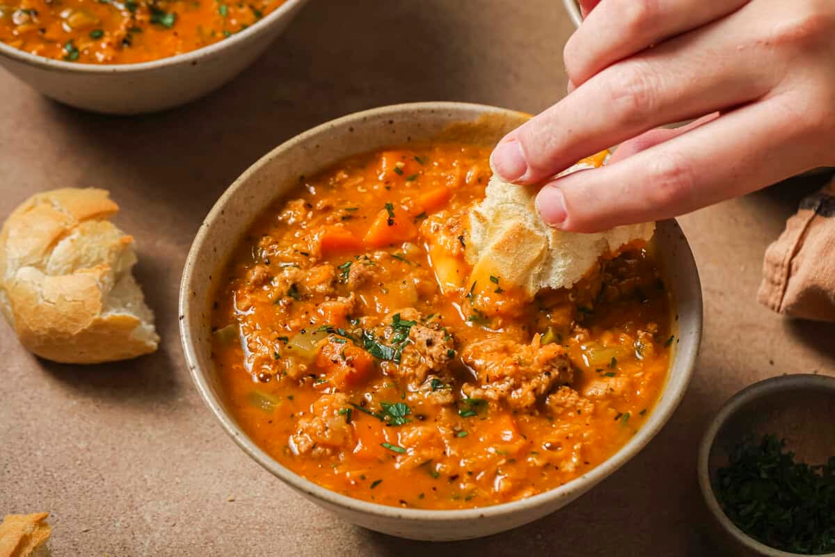 bowl of lentil sausage soup with bread being dipped in it