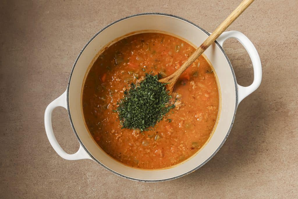 parsley being added to a cooked red lentil and sausage soup 