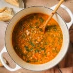 a bowl of lentil sausage soup with bread on table