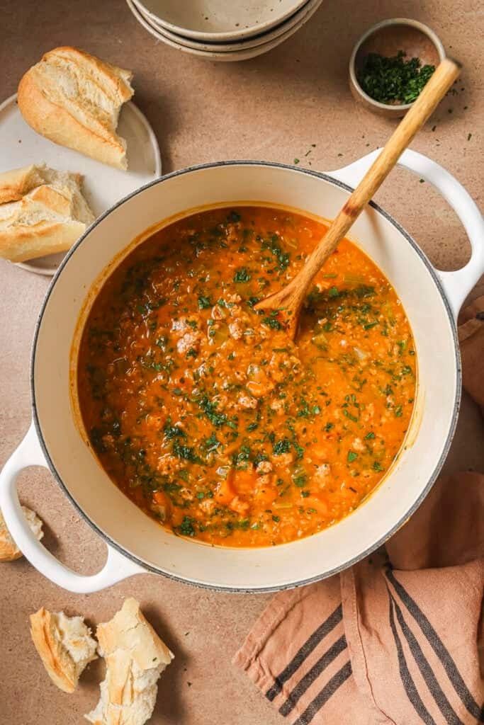 a bowl of lentil sausage soup with bread on table